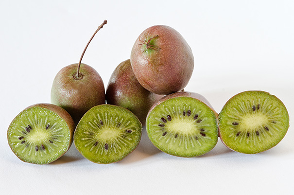 seven kiwi 'Prolific' with green and red skin, cut in half to show the inside