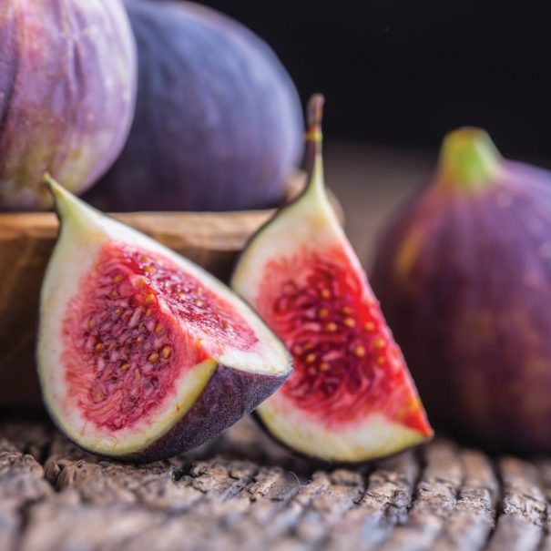 Chicago Hardy Figs in a bowl on a wooden table, close-up focus on one fig that has been quartered.